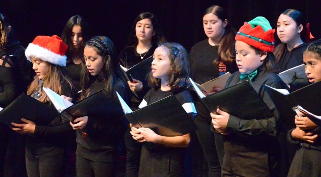 A group of childern singing, holding sheet music.